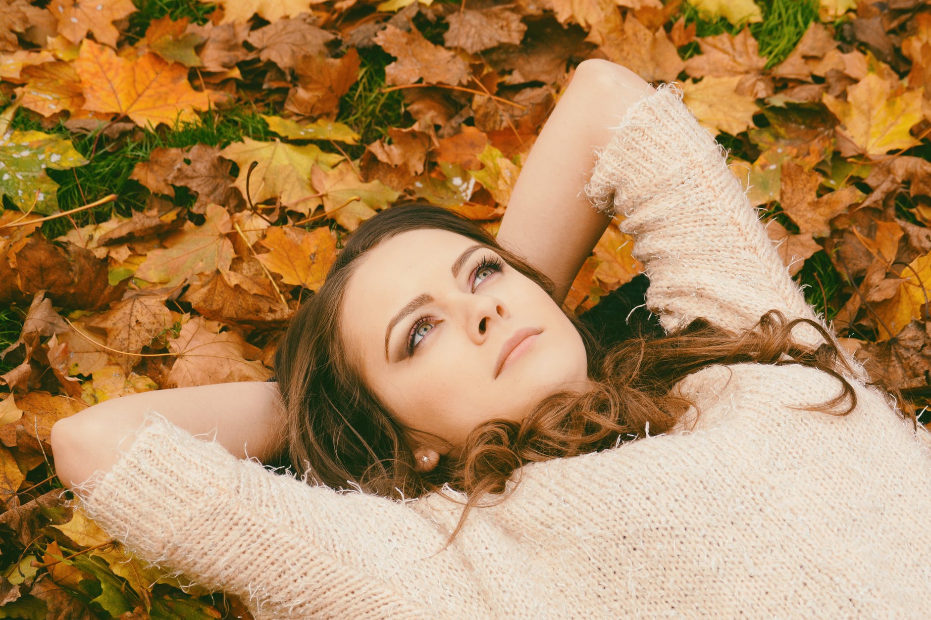 woman in sweater laying on dried maple leaves